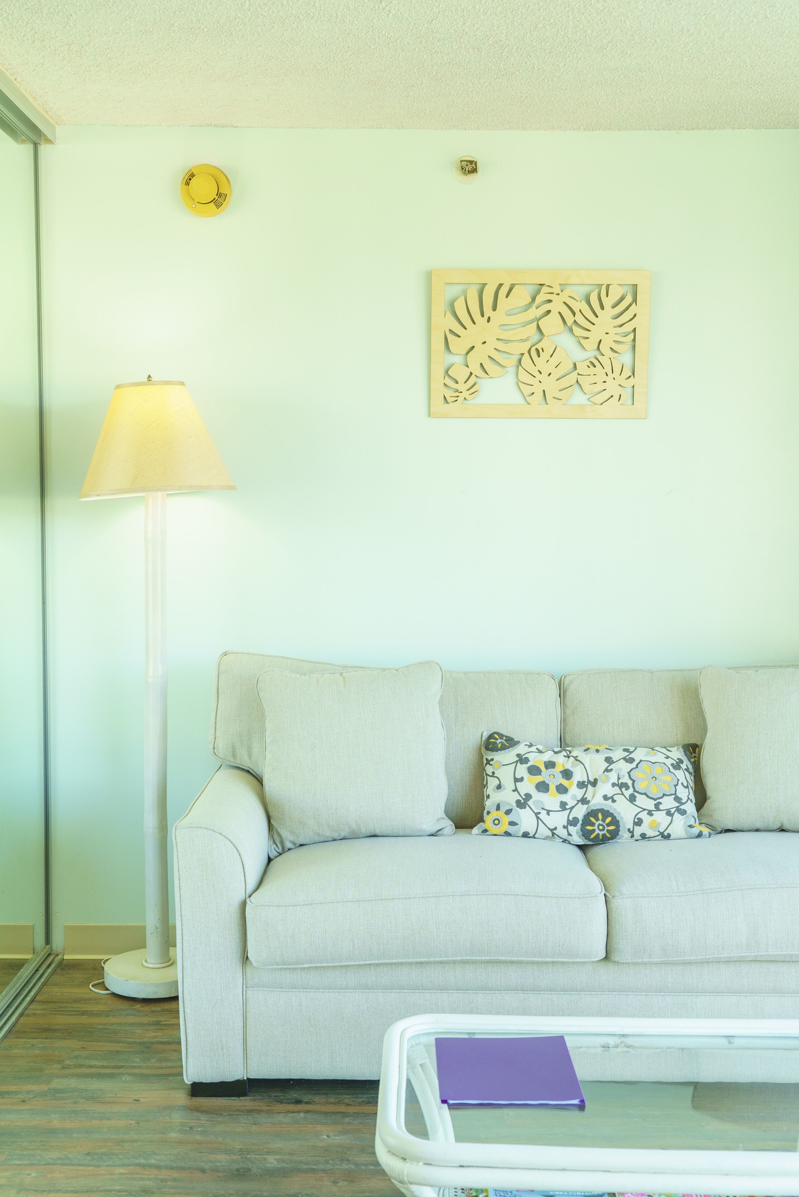 A room with a light-colored sofa, a floor lamp, a decorative wall piece, and a small table with a book.