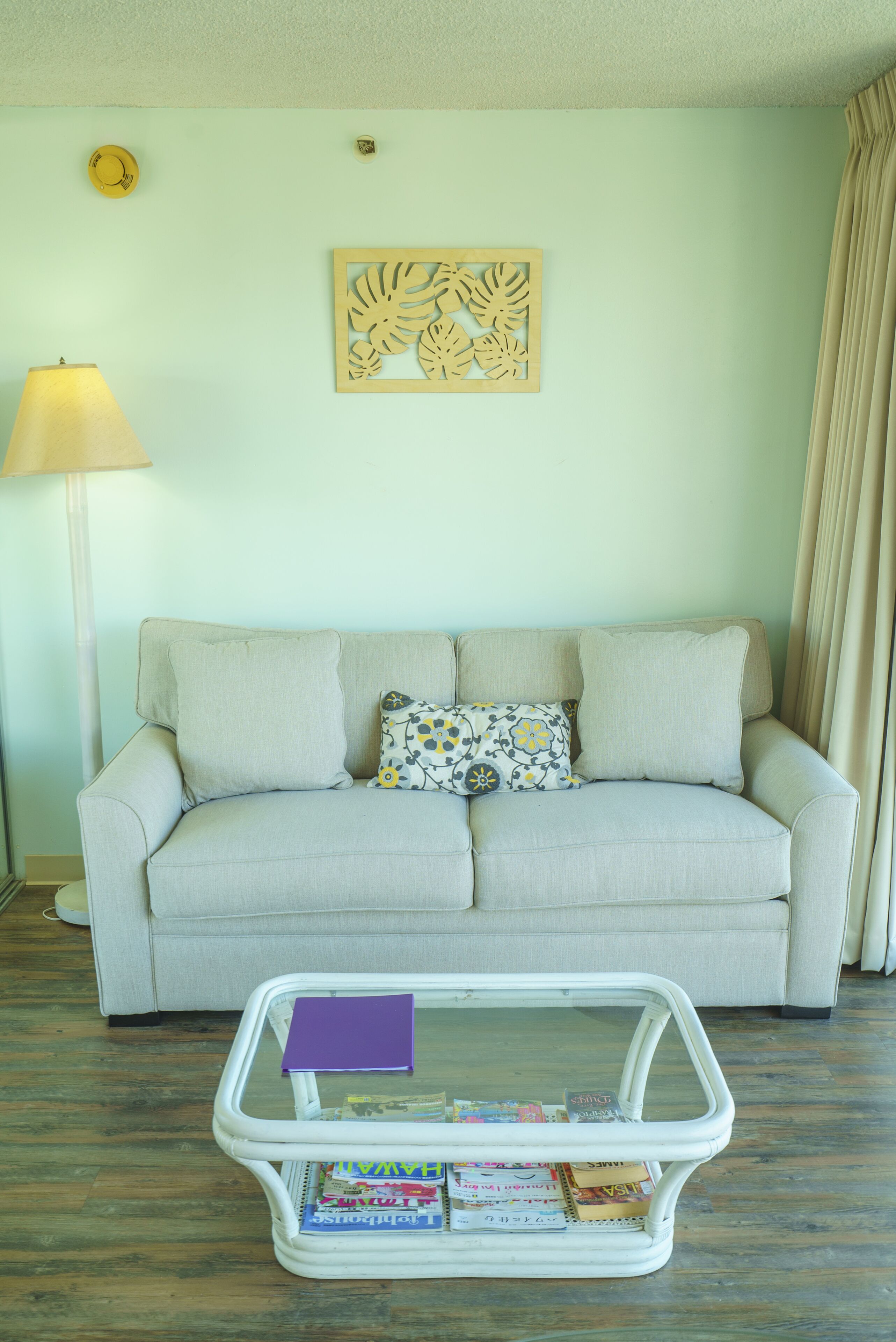 A living room with a sofa, a lamp, a decorative wall piece, and a magazine holder.