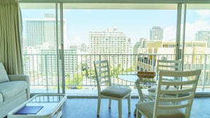 A modern living room with a glass coffee table, white chairs, and a view of a cityscape through large windows. - The Best Rate Ever!! Pacific Monarch Partial Ocean View Room!! (PM04) (Honolulu)
