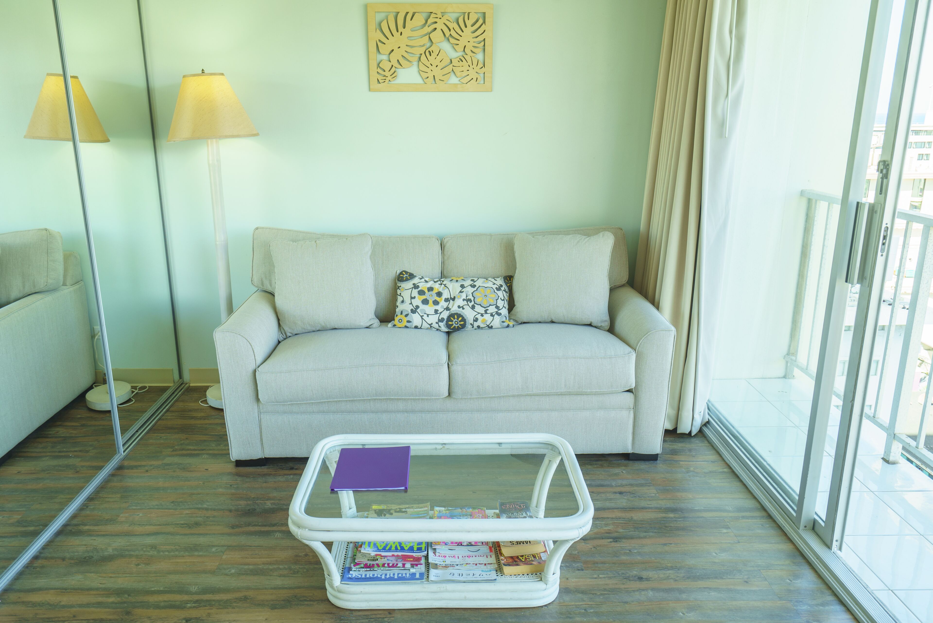 Sala de estar com sofá, mesa de centro com revistas, luminária de chão e janela com cortinas.