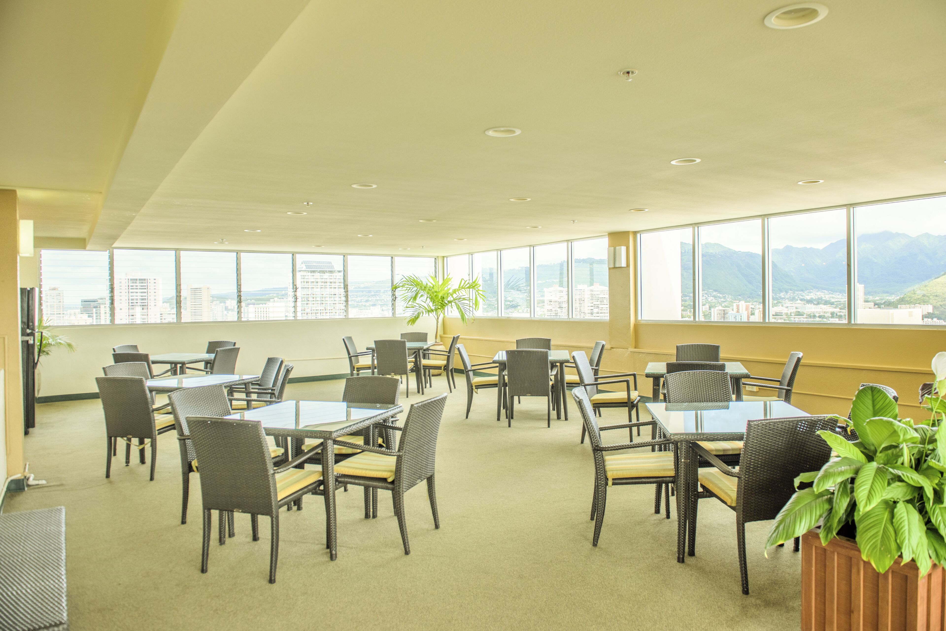 A spacious indoor area with multiple tables and chairs, large windows offering a city and mountain view, and a potted plant.
