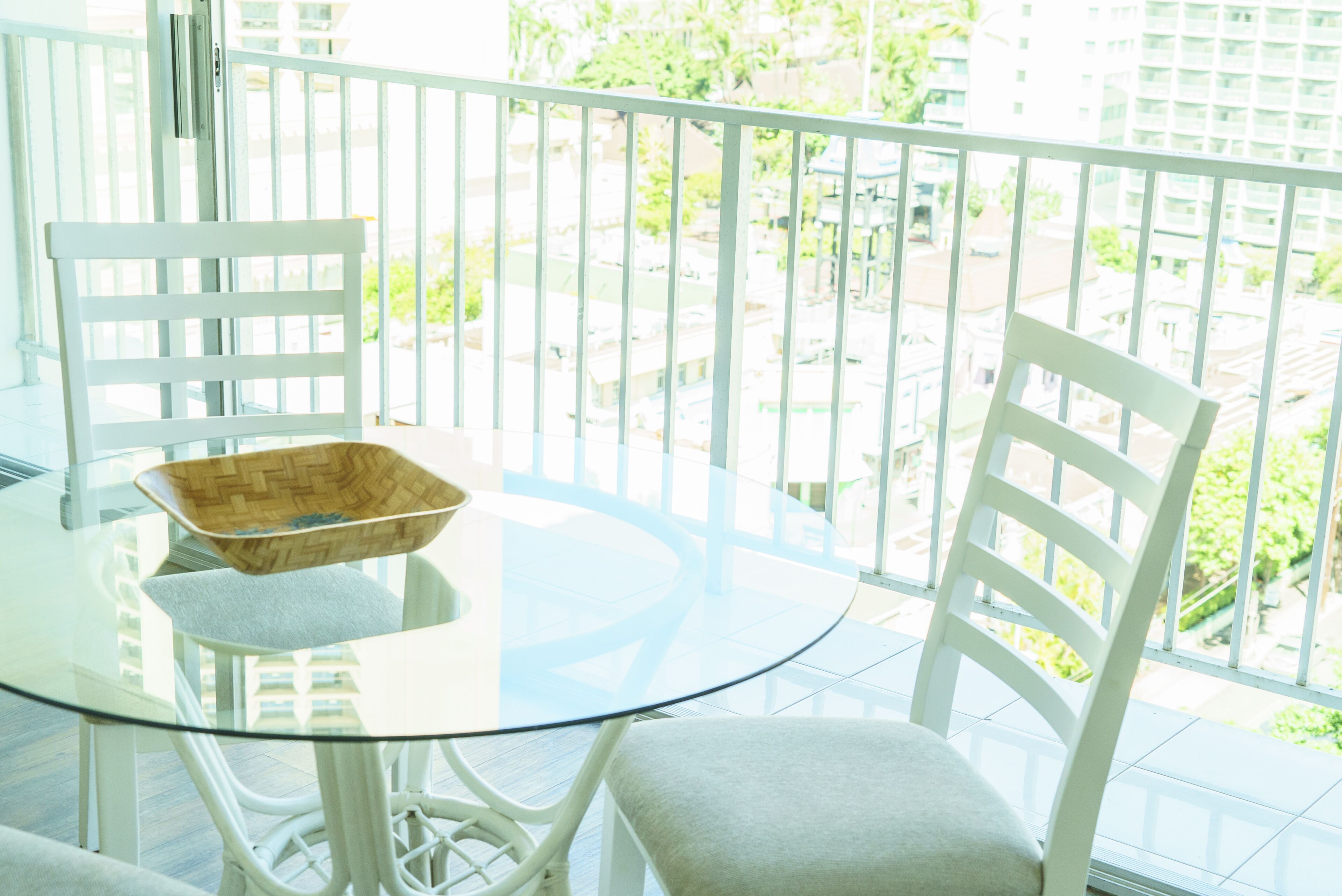 Un balcón con una mesa de vidrio y sillas blancas, con vistas a una zona residencial.
