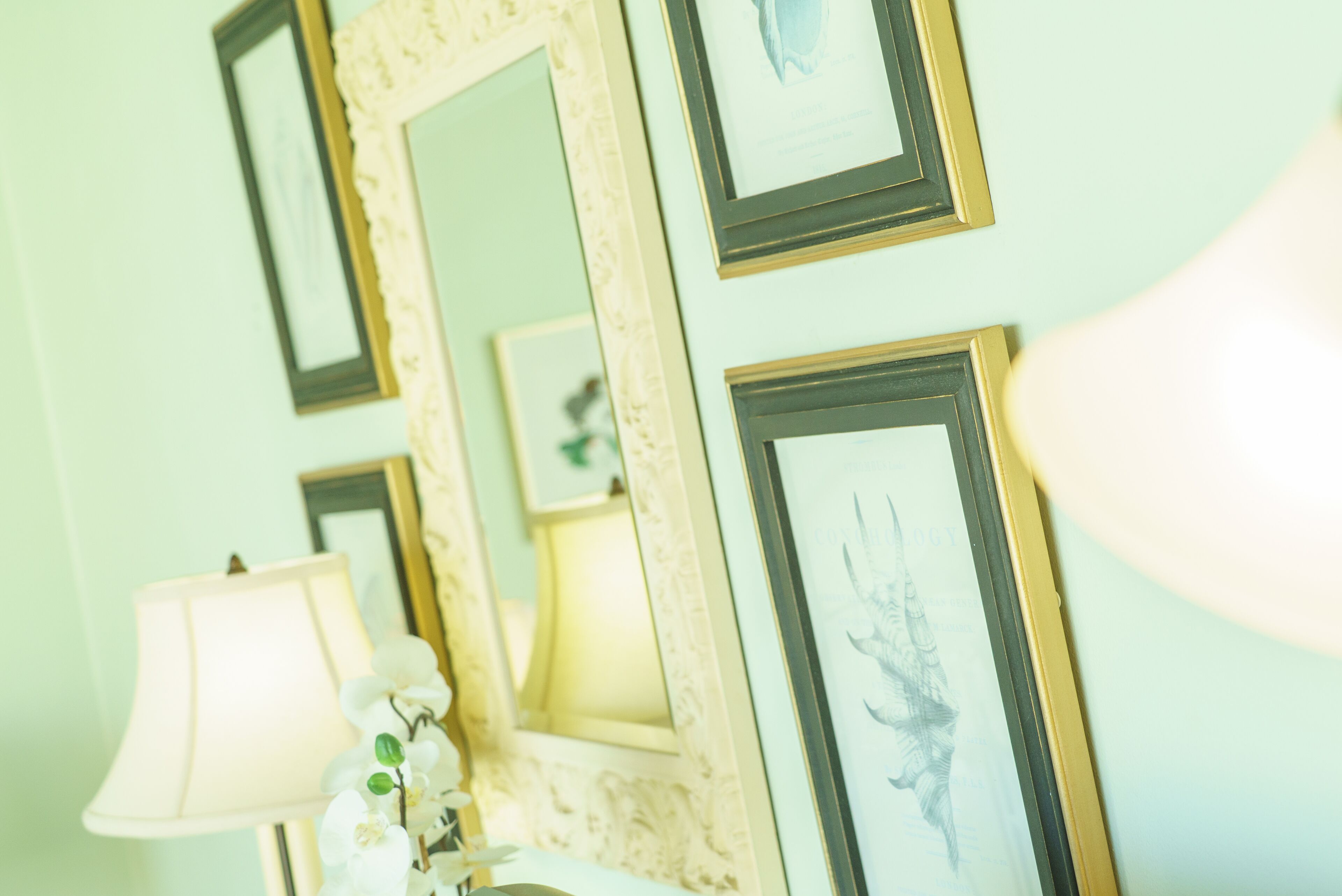 A wall with multiple framed pictures and a lamp.