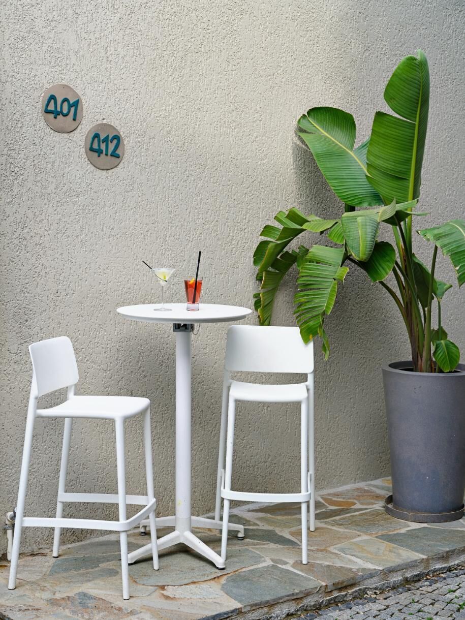 Een klein terras met twee witte stoelen en een ronde tafel, een plant in pot en twee getallen op de muur.
