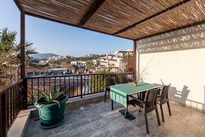 Un balcón con una mesa y sillas, una planta en maceta y vistas de edificios a lo lejos.