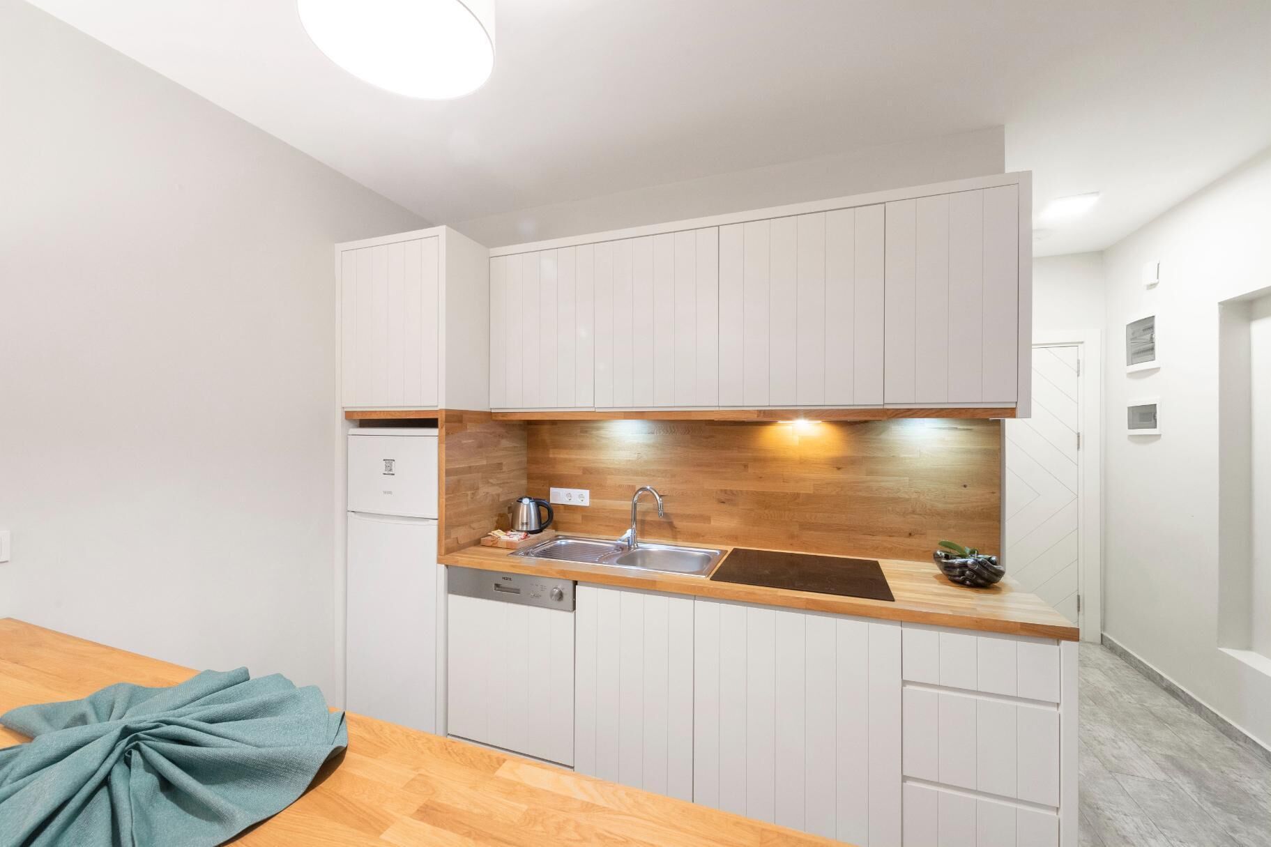 A compact kitchen with white cabinets, a wooden countertop, and a built-in dishwasher.