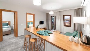 Une chambre d’hôtel moderne avec un coin repas en bois, un lit avec une literie de couleur turquoise, une télévision et une vue sur l’extérieur.