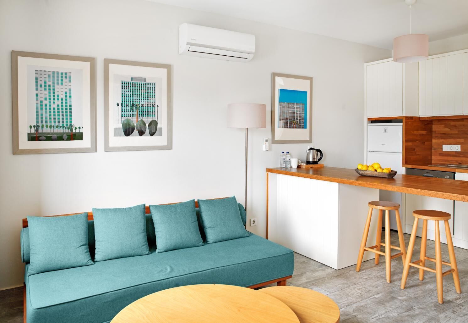 Un salon moderne avec un canapé de couleur turquoise, une table basse en bois et un coin cuisine doté d’un comptoir en bois et de tabourets de bar.