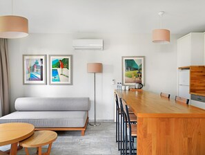 Ein modernes Hotelzimmer mit Sofa, Esstisch, Küchenzeile und zwei gerahmten Bildern an der Wand.