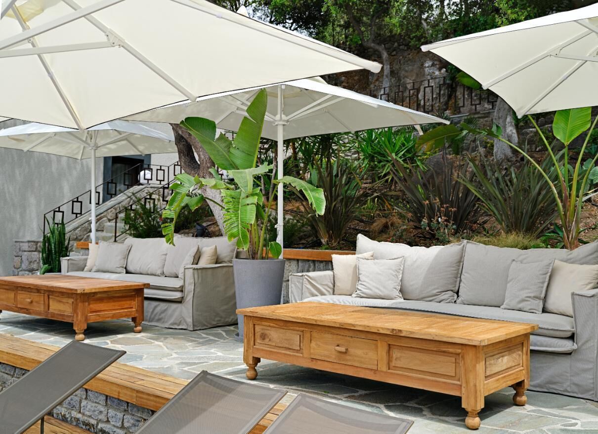 Un patio amueblado al aire libre, con sofás y una mesa de centro de madera, y sombrillas blancas.