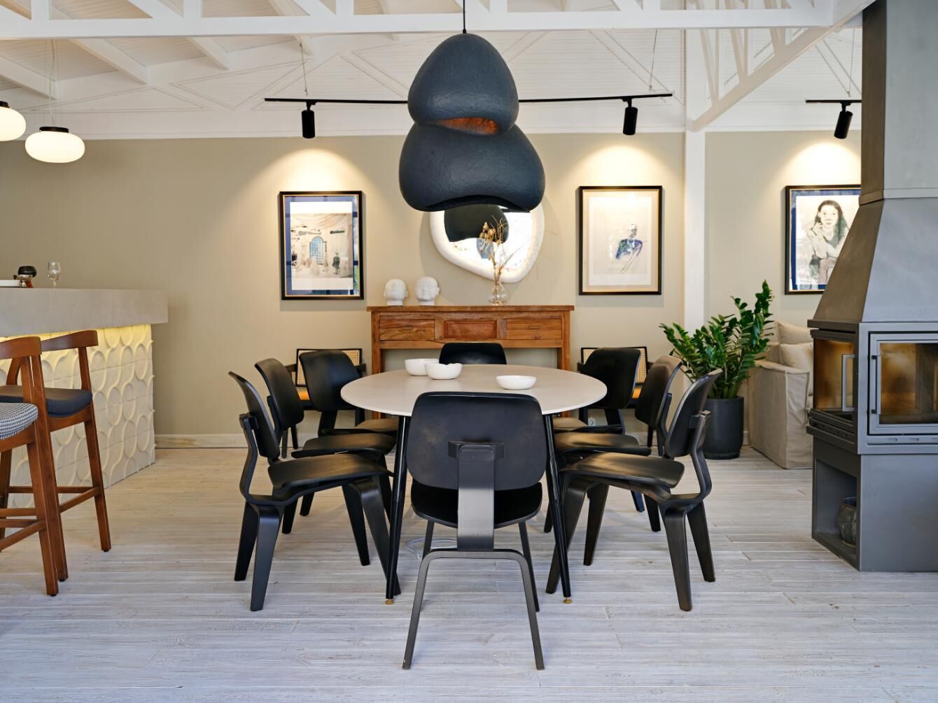 Een moderne eetruimte met een ronde tafel en stoelen, een houten bar en een ingebouwde grillplaats.