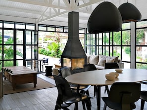 A modern interior with a large fireplace, black chairs, a round table, and large windows offering a view of greenery outside. - Dorman Suites Hotel (Bodrum)