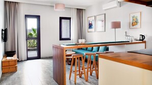 Quarto de hotel moderno com cozinha, mesa de jantar com banquetas, sofá e vista para o exterior.