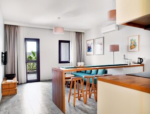 A modern hotel room with a kitchen area, a dining table with stools, a sofa, and a view of the outdoors. - Dorman Suites Hotel (Bodrum)