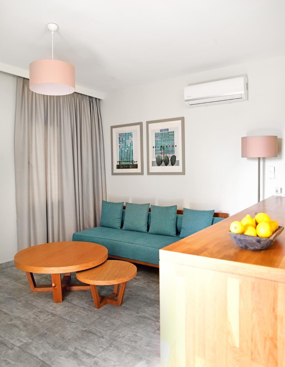 A modern living room with a sofa, two wooden tables, a bowl of lemons, and two framed artworks on the wall.