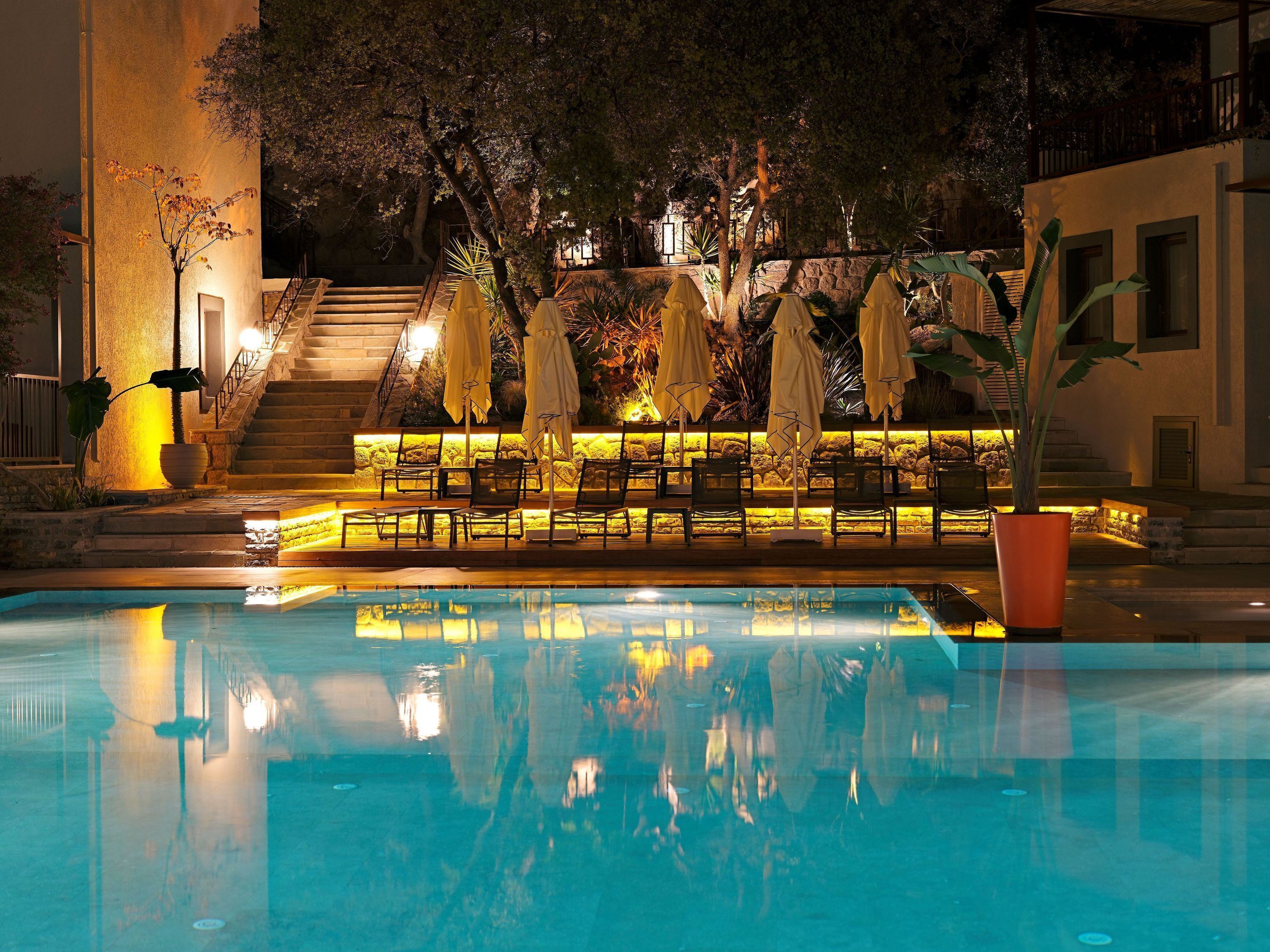 A nighttime pool area with lounge chairs and umbrellas, a stone staircase, and a building in the background.