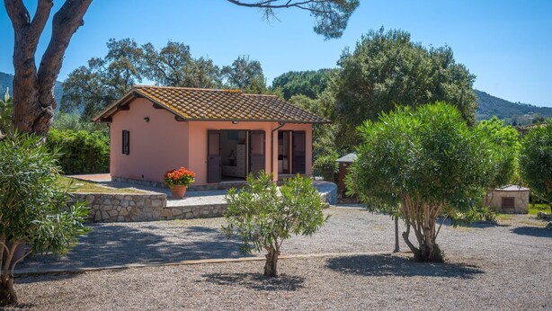 Uma pequena casa com telhado de telhas, caminho de pedra e área com brita.