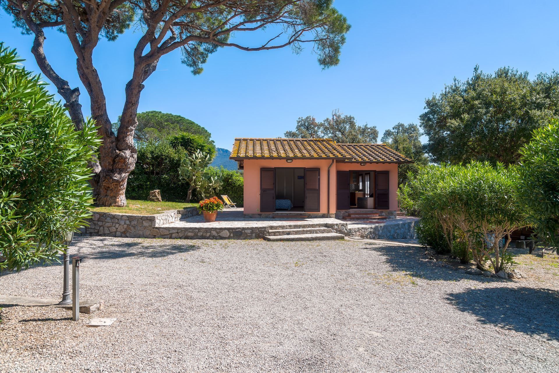 A small, single-story building with a tiled roof, surrounded by gravel and greenery.