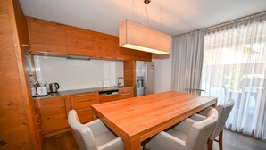 Une cuisine moderne avec des meubles en bois, un réfrigérateur en acier inoxydable et une table à manger en bois, assortie de chaises blanches.