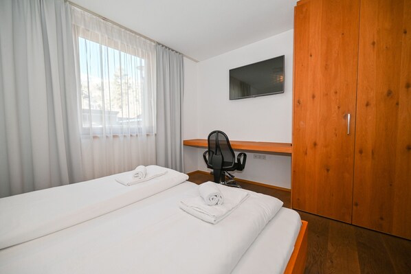 A hotel room with two beds, a desk, a TV, and a wardrobe.