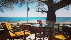 Un patio con sillas de mimbre y una mesa, con vistas a una playa y al mar.