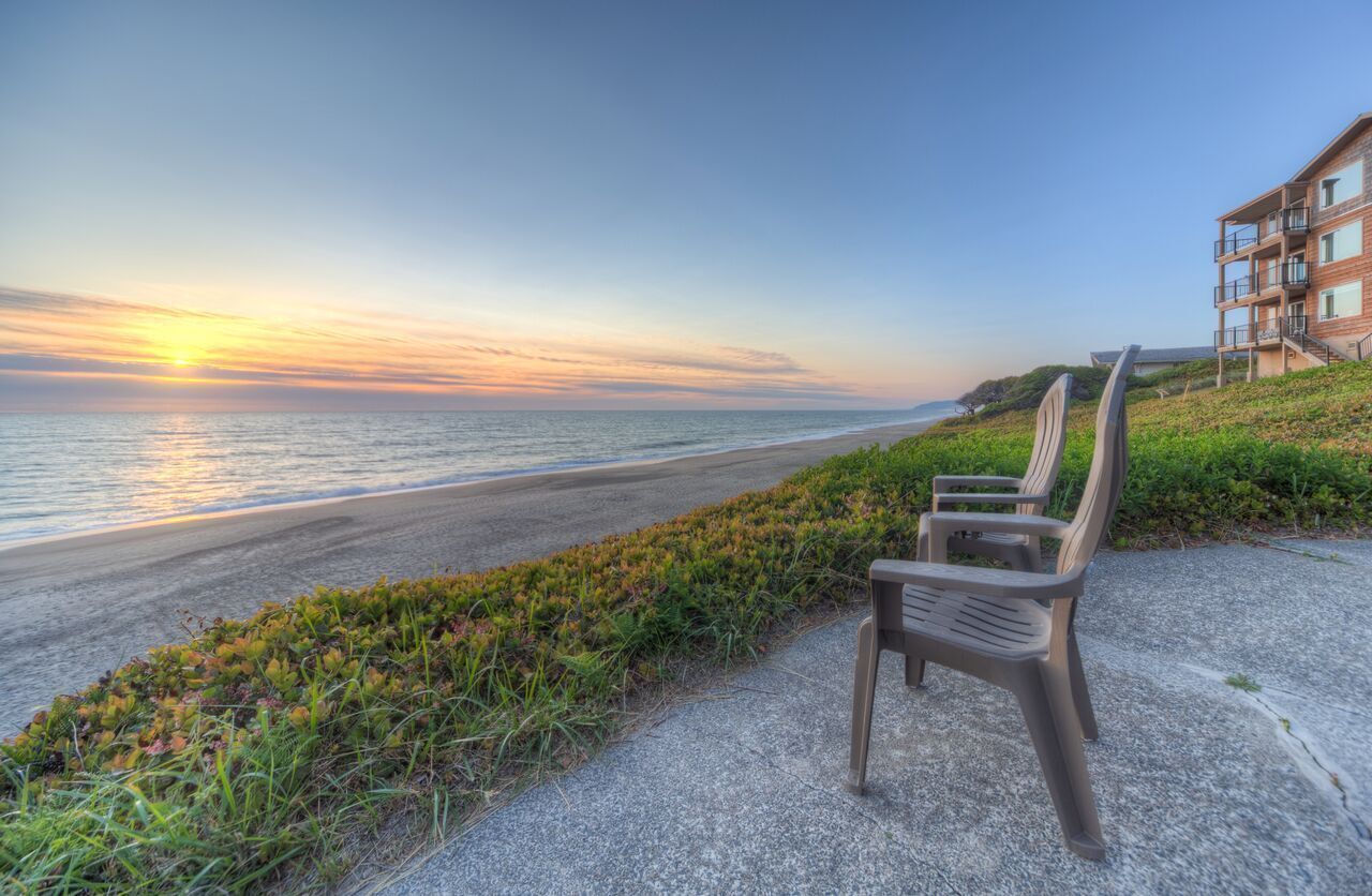 Un banc au bord de la plage, avec vue sur l’océan et un bâtiment en arrière-plan.
