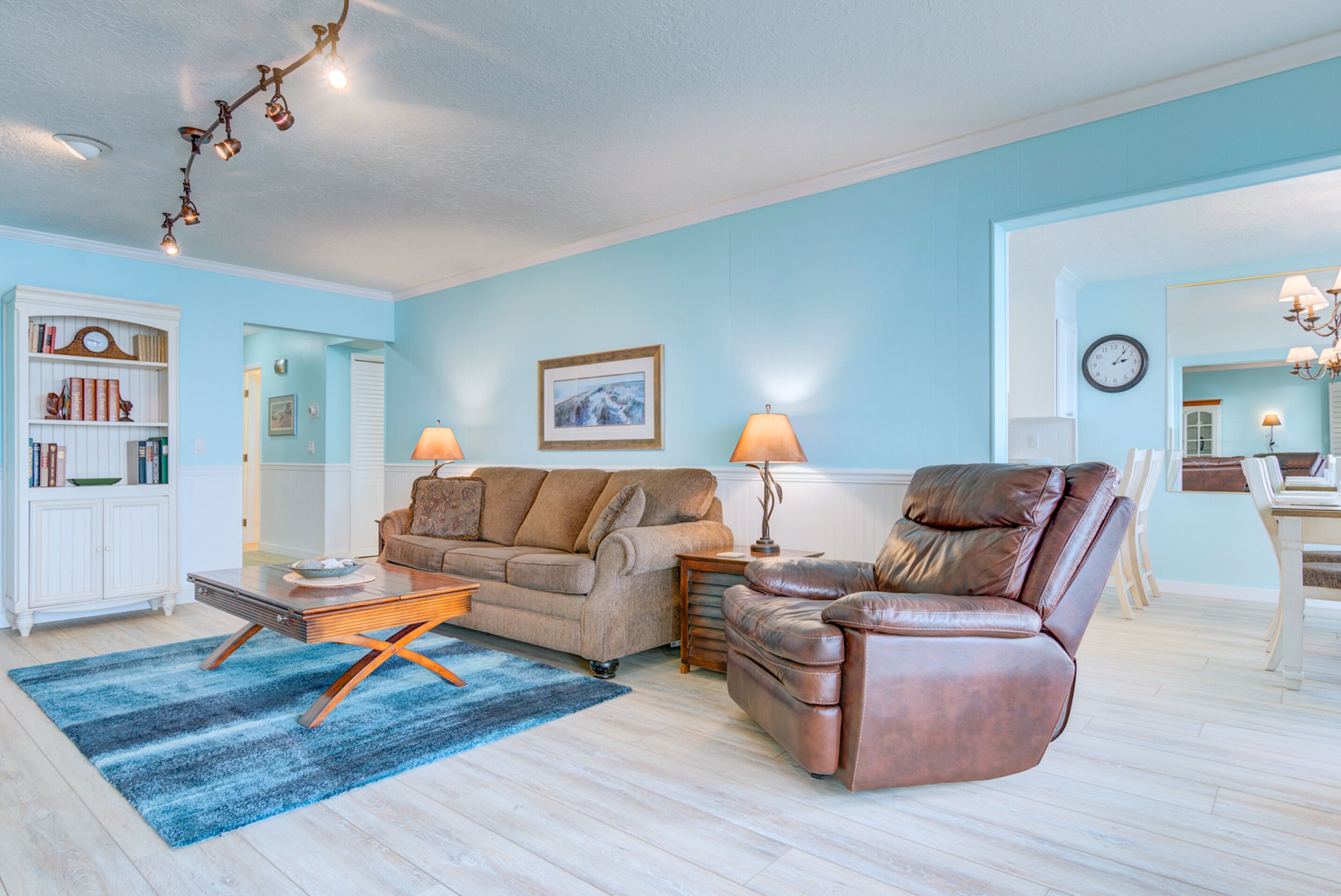 Ein Wohnzimmer mit blauer Wand, einem braunen Ledersofa, einem braunen Ledersessel, einem Holztisch und einem blauen Teppich.