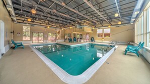 Une piscine intérieure à l’eau claire, entourée de murs de couleur beige et dotée d’un plafond haut avec des poutres apparentes.