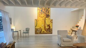Ein geräumiges Wohnzimmer mit einem großen abstrakten Gemälde an der Wand, Holzboden und einer Treppe, die zu einer weiteren Ebene führt.
