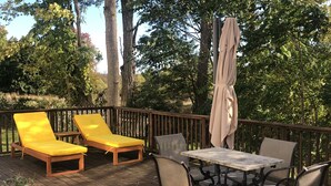 Eine Holzterrasse mit gelben Liegestühlen, einem Tisch mit Stühlen und einem Sonnenschirm.