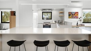 Une cuisine moderne dotée d’un grand îlot central, de tabourets de bar et d’une fenêtre offrant une vue sur les arbres.