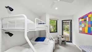 Une chambre avec un lit superposé, une fenêtre, un bureau et une œuvre d’art colorée accrochée au mur.