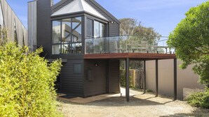 Une maison moderne à deux étages, dotée d’une grande baie vitrée, d’une terrasse en bois et d’un jardin clôturé.
