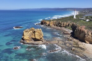 A coastal landscape with a prominent rock formation, a lighthouse, and a clear view of the ocean.