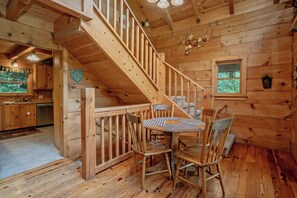 Interior de una cabaña de madera con comedor, escalera y cocina.