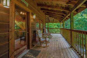 A wooden deck with a railing, a covered porch, and a view of the surrounding forest. - Knotty And Nice: Seclusion, Pets, HotTub, Wifi, Games, close to the Park (Pigeon Forge)