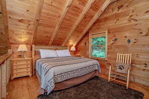Een slaapkamer in een houten blokhut met een bed, nachtkastjes, een raam en een stoel.