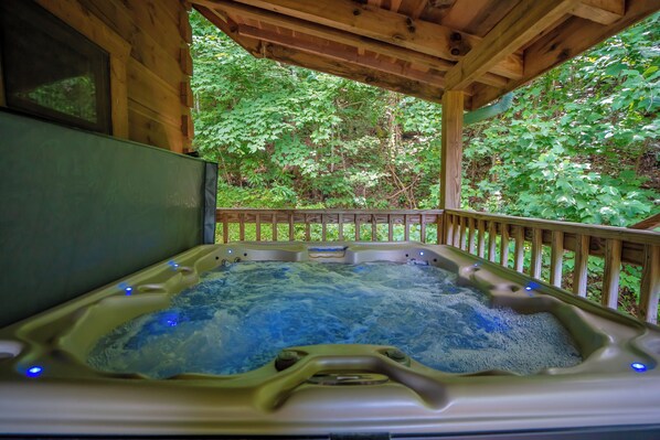 Un jacuzzi con terraza de madera y vista a un bosque verde exuberante.