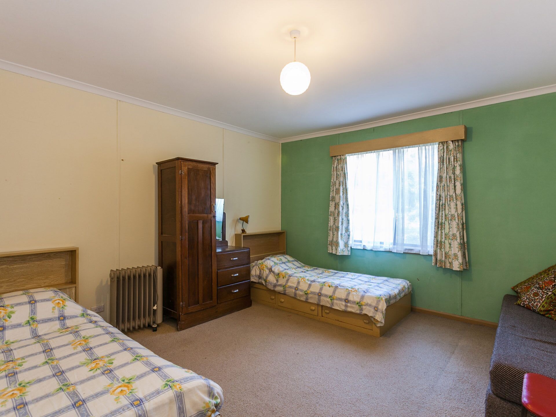 A bedroom with two beds, a wardrobe, a radiator, and a window with curtains.