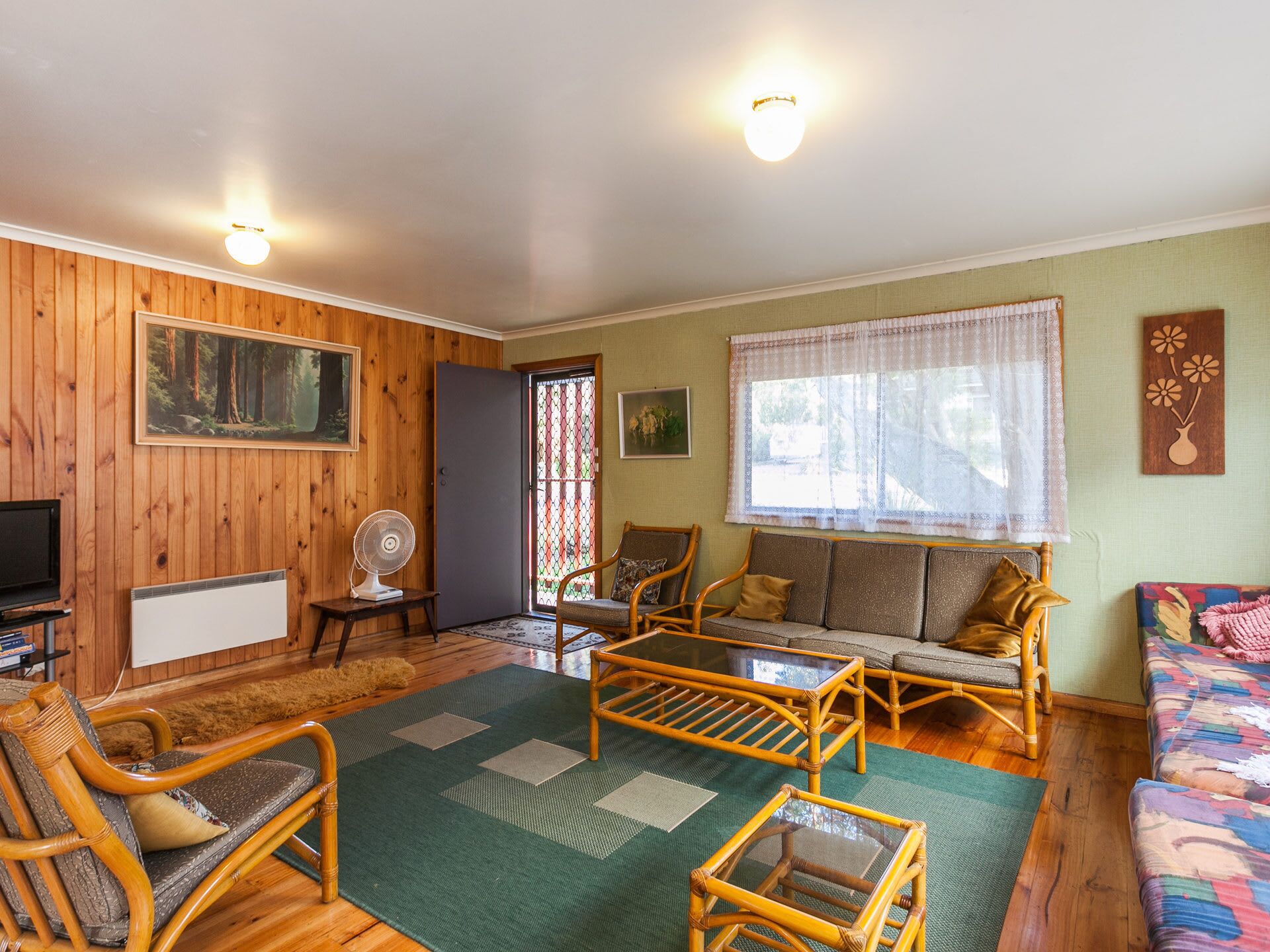 A cozy living room with wooden walls, a sofa, two armchairs, a coffee table, and a television.