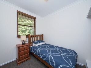 A bedroom with a single bed, a nightstand, a lamp, and a window with blinds.