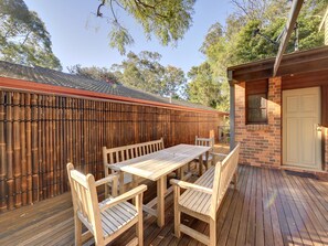 Een houten terras met een tafel en stoelen, een bakstenen muur en een deur.