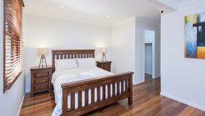 A bedroom with a wooden bed, two bedside tables, a lamp, and a painting on the wall. - Barefoot Beach House Shoal Bay Retreat (Shoal Bay)