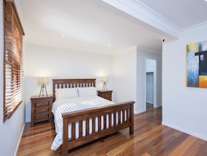 Een slaapkamer met een houten bed, twee nachtkastjes, een lamp en een schilderij aan de muur.