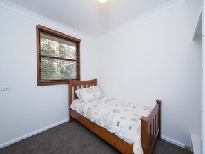 A small, single-bed room with a wooden headboard, a window with blinds, and a carpeted floor. - Barefoot Beach House Shoal Bay Retreat (Shoal Bay)