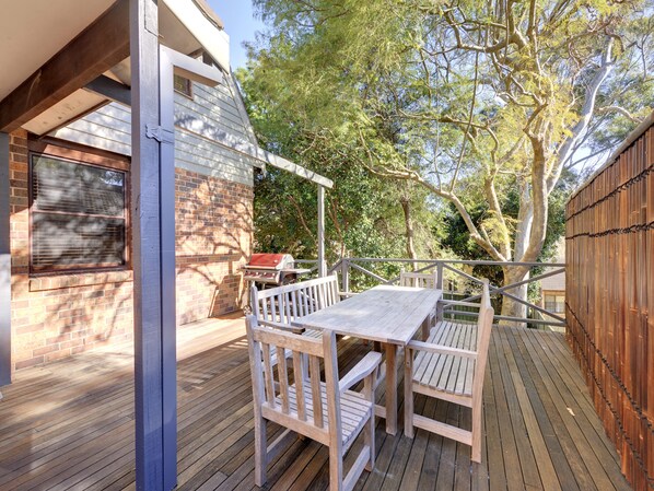 A wooden deck with a table and chairs, a barbecue grill, and a brick wall.