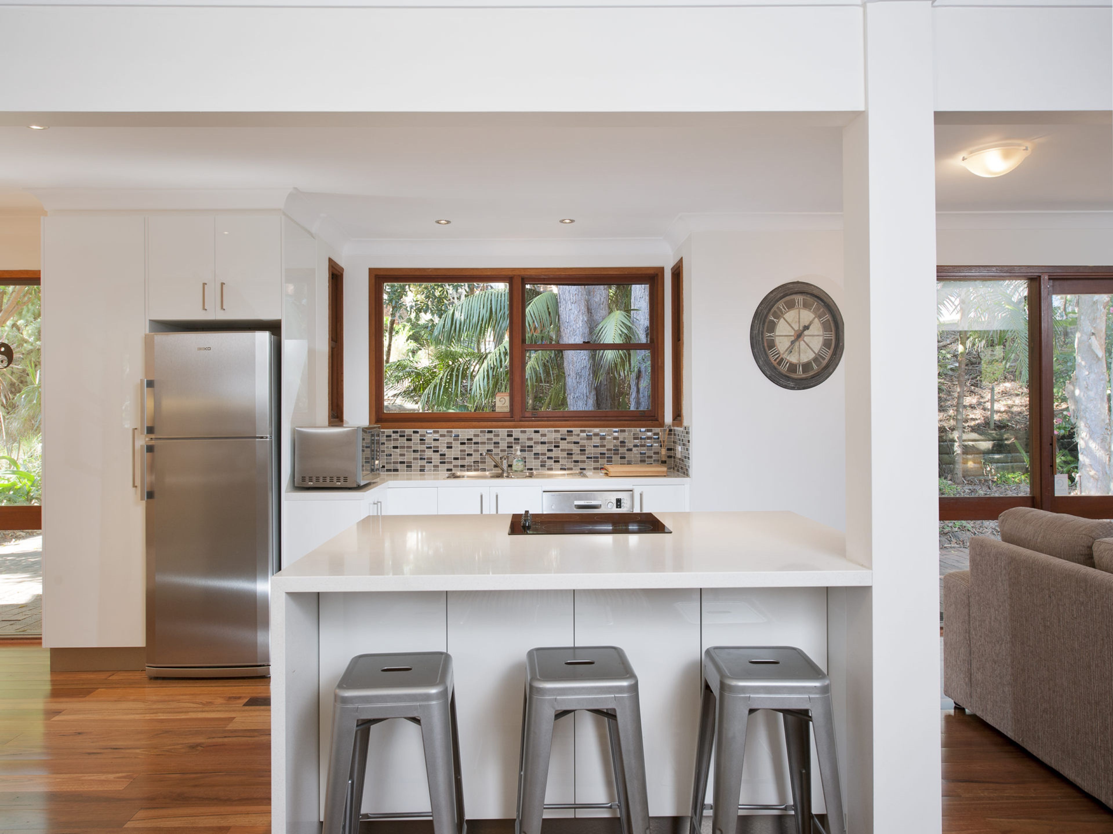 Una cocina moderna con un refrigerador de acero inoxidable, un lavamanos doble y un amplio ventanal con vistas a la vegetación.