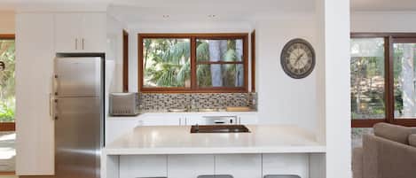 Una cocina moderna con un refrigerador de acero inoxidable, un lavamanos doble y un amplio ventanal con vistas a la vegetación.