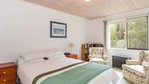 Een slaapkamer met een groot bed, een stoel, een boekenkast en een raam met uitzicht op bomen.
