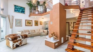 Un vaste espace de vie doté d’un haut plafond, d’un escalier moderne et d’un balcon agrémenté de plantes.